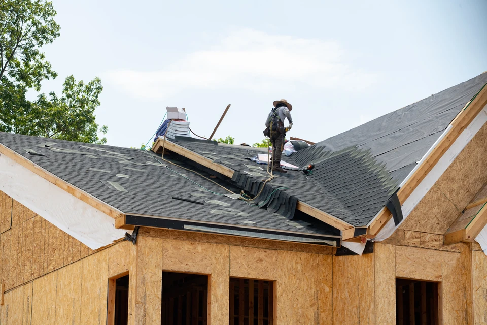 Chantier de construction résidentielle en extérieur avec ouvrier couvreur travaillant sur toiture en pente