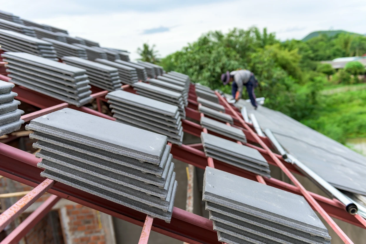Chantier de toiture en cours avec ouvrier installant des tuiles plates grises sur charpente à structure métallique rouge