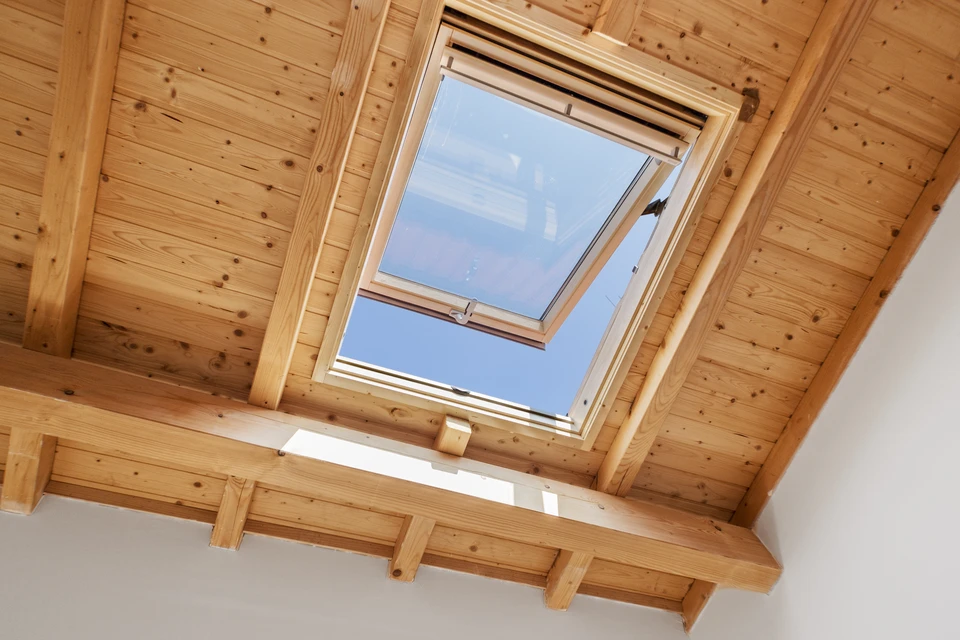 Intérieur d'un comble aménagé avec fenêtre de toit ouverte laissant voir le ciel bleu nuageux