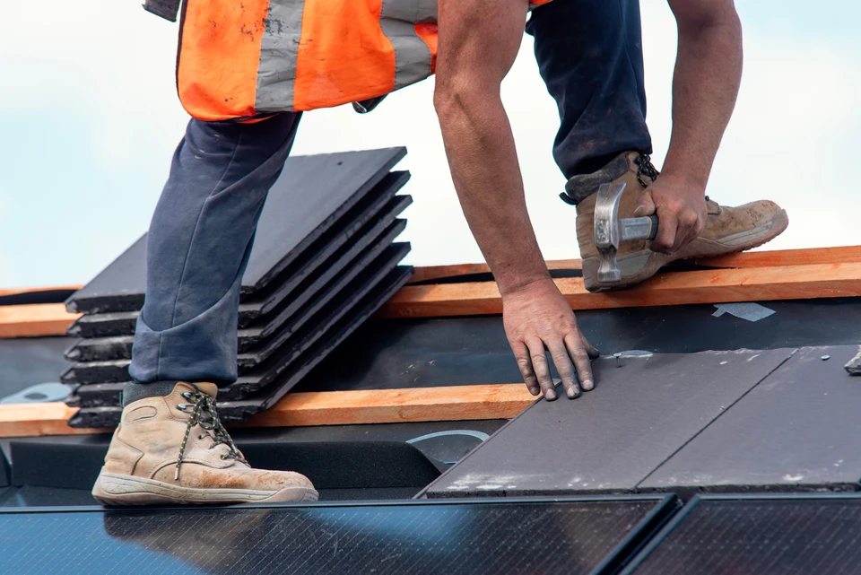 Ouvrier en &eacute;quipement de s&eacute;curit&eacute; installant de l'isolation thermique entre chevrons de toiture dans combles en construction