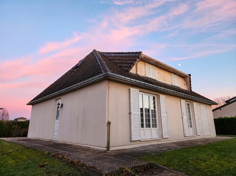 Vue en contre-plongée d'une façade extérieure enduite, couleur beige sable, avec gouttière cylindrique en zinc satiné fixée en rive de toiture plate