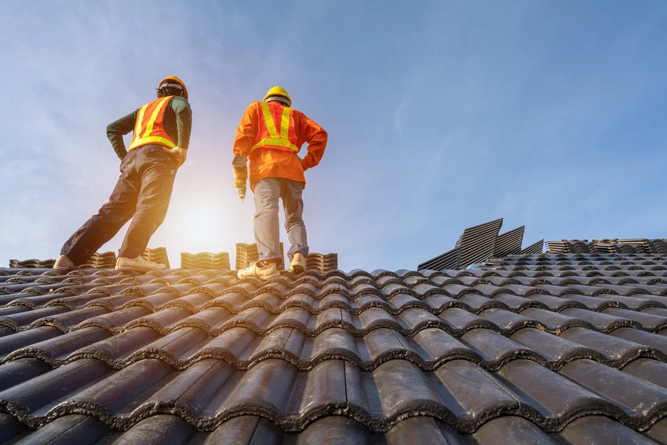 Deux couvreurs professionnels travaillent sur une toiture en chantier au coucher du soleil