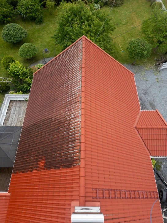 Deux couvreurs travaillent sur une toiture en pente, installant des tuiles terre cuite rouge sur charpente bois